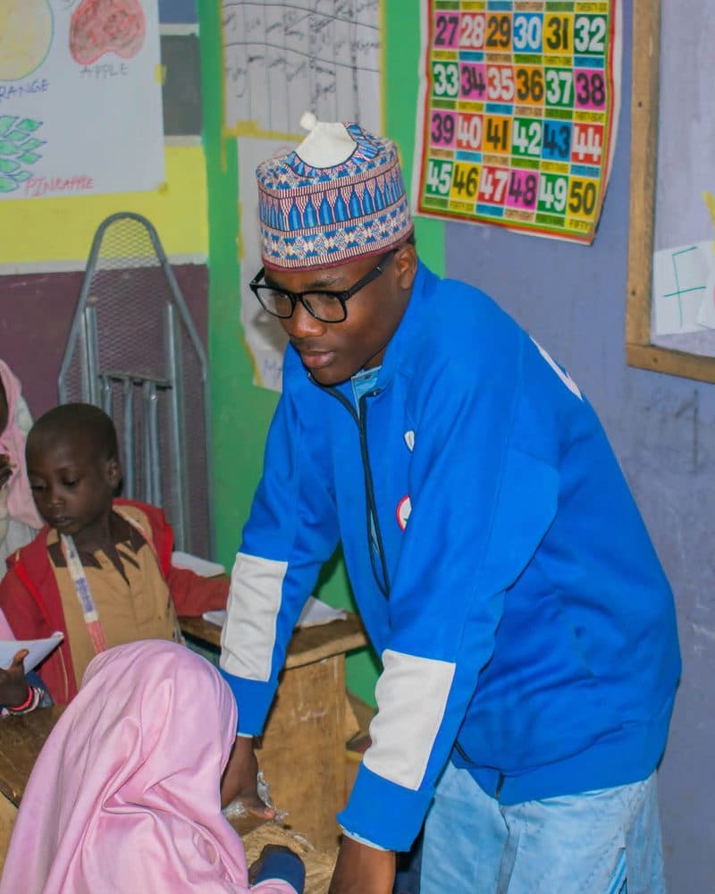 A teacher leaning over a desk to help pupils in a brightly decorated classroom