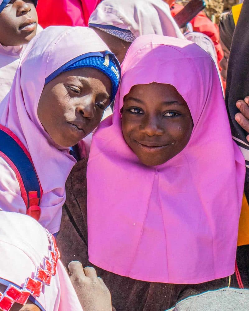 Two pupils in pink and blue uniform smiling among a crowd of classmates