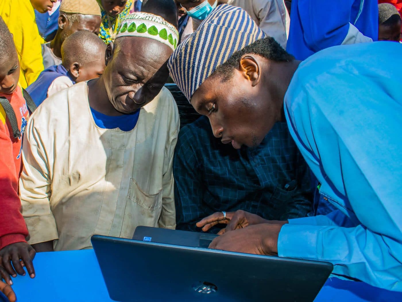 A facilitator guiding two older community members through a task on a laptop