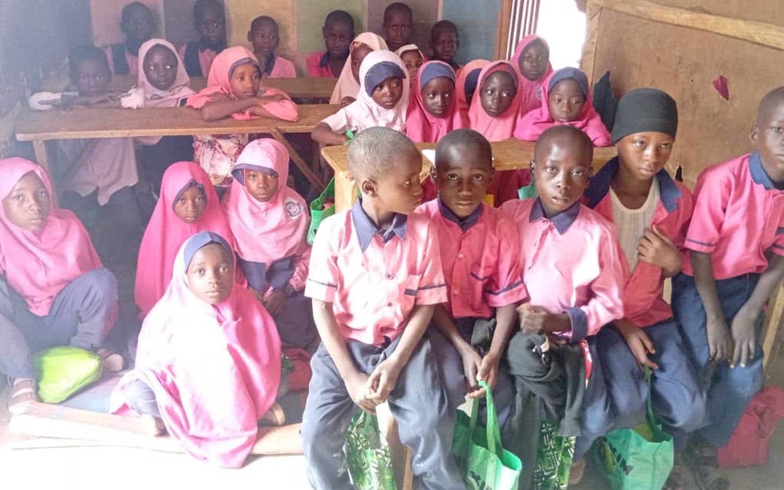 A full classroom of pupils in pink and blue uniform seated at benches